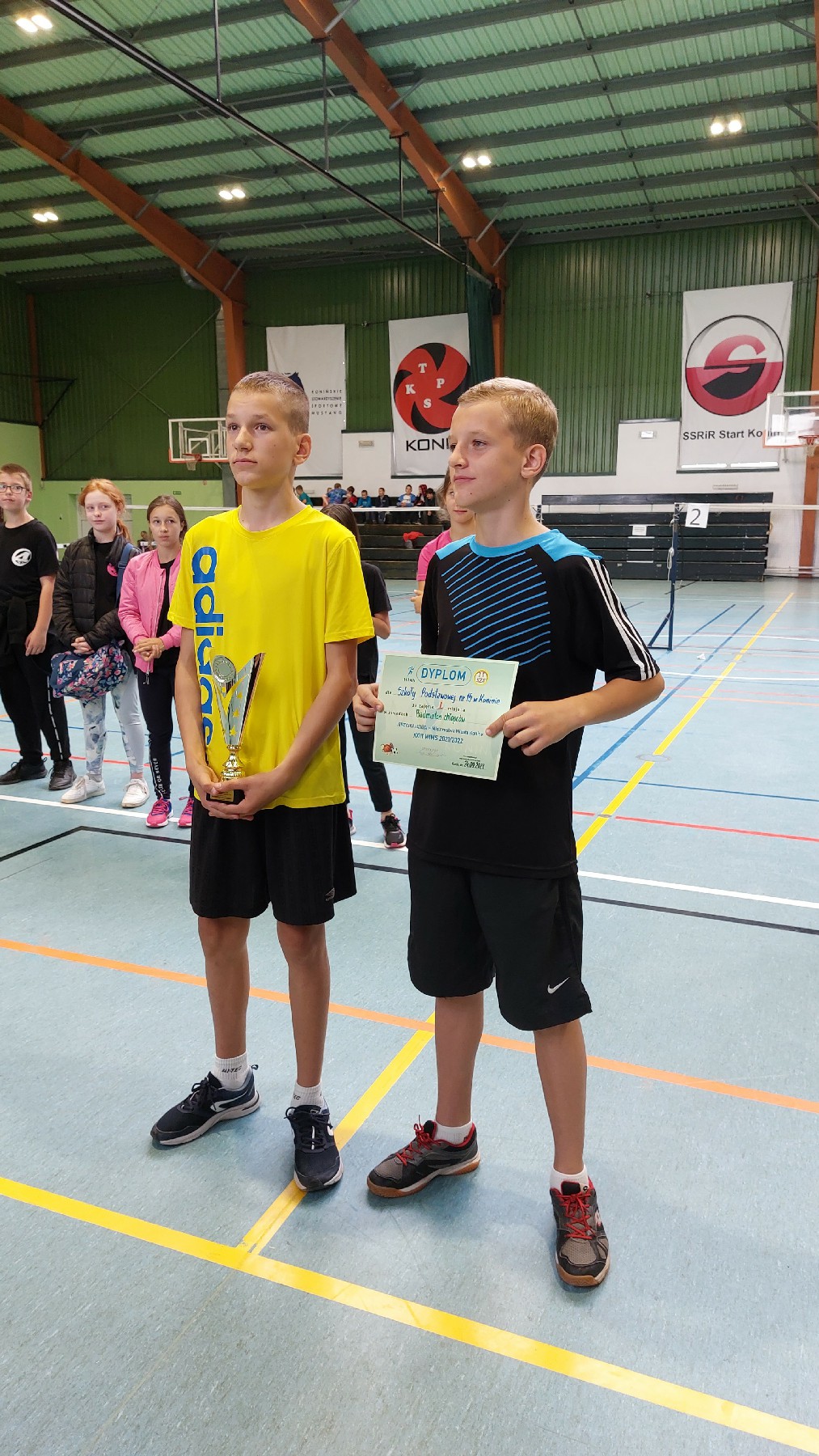 Dwóch chłopców, zwycięzców zawodów sportowych w badmintonie z pucharem i dyplomem. 